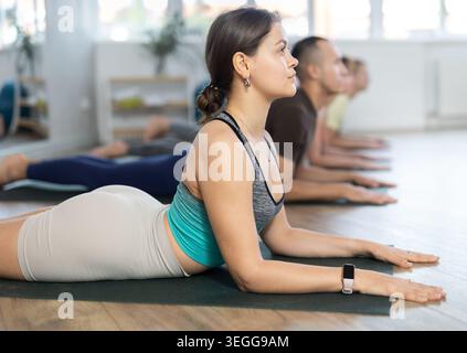 Sporty woman and man practicing yoga positions during group training in fitness center, performing stretching asana Urdhva Mukha Shvanasana Stock Photo