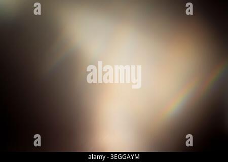 Dark moody abstract background featuring a warm glowing light leak and vibrant rainbow prism effect Stock Photo