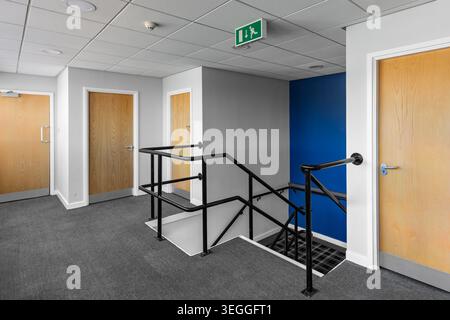 Interior view of commercial office landing and stairwell with carpet flooring, modern doors and emergency exit sign in professional workplace setting Stock Photo