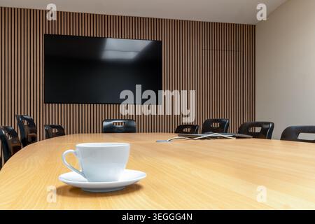Modern boardroom or conference room with large meeting table, presentation screen and coffee cup in professional business and corporate office environ Stock Photo