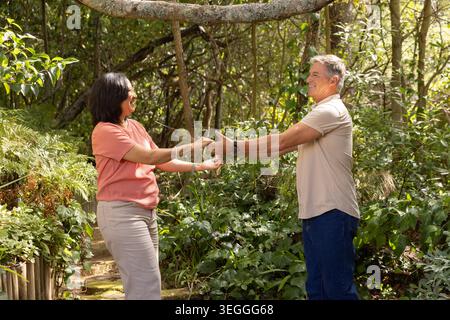 Mature couple standing holding hands on garden path by wooden railing, showing wristwatch, bracelet Stock Photo