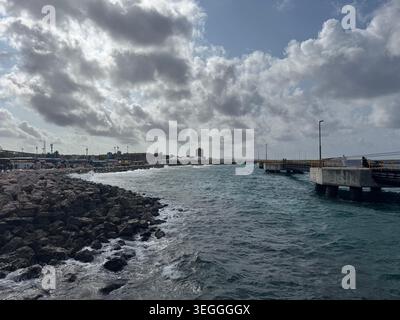 Scenic view of the dark blue ocean waves crashing against the rocky coastline and pier under a dramatic cloudy sky in Curacao. Stock Photo