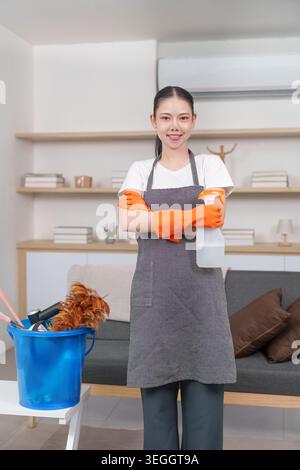 Confident Asian woman with cleaning supplies in home office Stock Photo