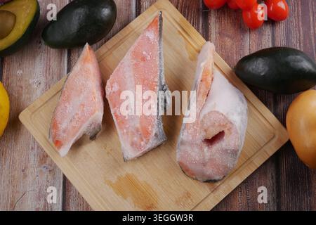 Frozen fish slices on cutting board with fresh produce Stock Photo