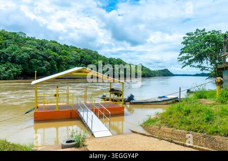 A bright yellow dock extends over the calm water, surrounded by dense greenery and under a partly cloudy sky in Colombia’s Guaviare region. Stock Photo