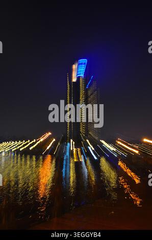 A dynamic, abstract night shot of a skyscraper illuminated with neon lights, with light trails streaking from its base, reflecting on a dark. Stock Photo