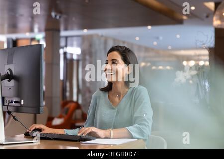 Smiling female receptionist working on computer at reception desk Stock Photo