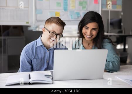 Man with Down syndrome and colleague working together on laptop Stock Photo