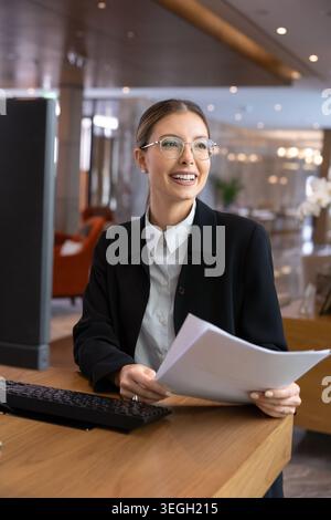 Smiling female hotel staff receptionist working at front desk Stock Photo