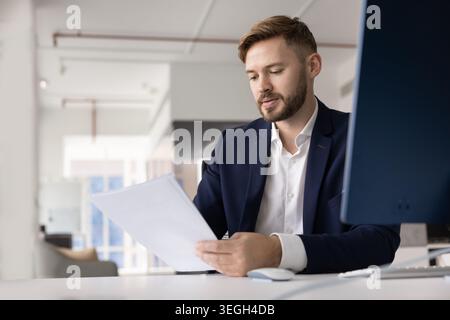 Focused young businessman reading and analyzing documents with serious expression Stock Photo