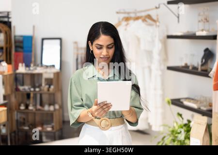 Young Indian woman using tablet in stylish fashion boutique Stock Photo