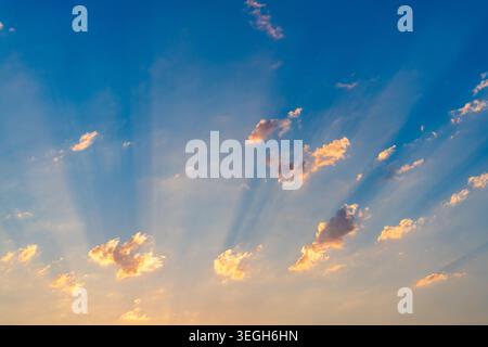 Golden hour sunlight streaming through fluffy clouds creates a breathtaking display in a vibrant blue sky, enhancing the serene and tranquil atmospher Stock Photo