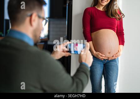 Multiethnic happy pregnant couple using mobile phone for vlogging, take photo, communicating online Stock Photo