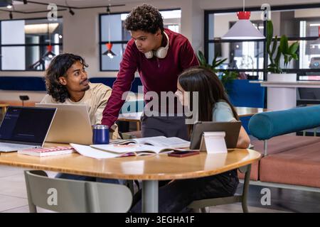 Diverse study group collaborating around round wooden table in modern lounge with laptops Stock Photo