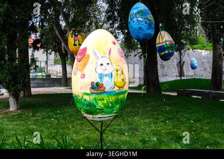 A whimsical display of oversized, brightly painted Easter eggs decorates a lush park, featuring a charming bunny and chick design. Stock Photo