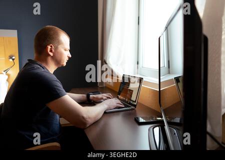 Man typing on a laptop, coding, working remotely from a hotel desk Stock Photo