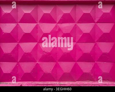 A close-up view of a textured concrete wall painted in a bright, bold pink hue, showcasing its repeating geometric design Stock Photo