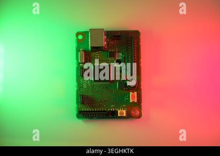 Colorfully lit circuit board (PCB) featuring a central microchip, connectors and electronic components on a red-to-green gradient background. Technolo Stock Photo