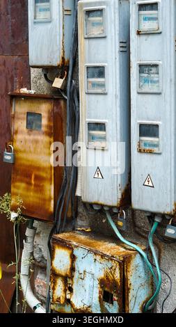 Old rusted electrical boxes and power meters mounted on a weathered outdoor wall Stock Photo