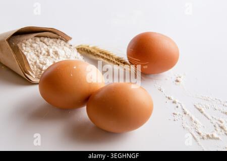 Brown chicken eggs with flour and wheat ears on white surface Stock Photo
