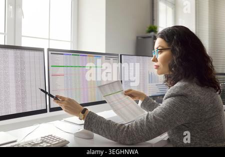 Woman accountant analyzing spreadsheets and reports on three computer monitors Stock Photo