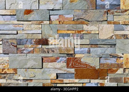 Wall cladding made of different sizes natural stones. Colors are shades of red, yellow and gray. Background and texture. Stock Photo