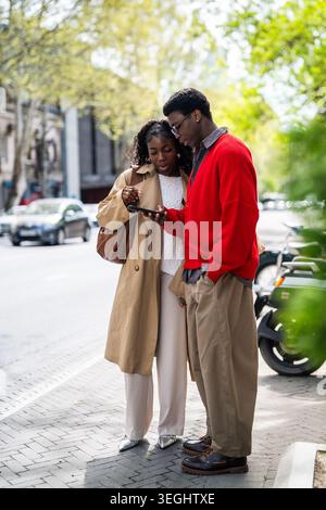 Stylish african american friends tourists checking city map on smartphone while ordering taxi in app Stock Photo