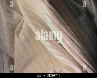 Close up of shimmering white textile fabric with soft folds and subtle iridescent glow, elegant material texture background with delicate highlights. Stock Photo