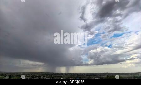 Dramatic storm cloud formation with visible rainfall in the distance above rural landscape, dark thunderclouds and changing weather atmosphere before Stock Photo