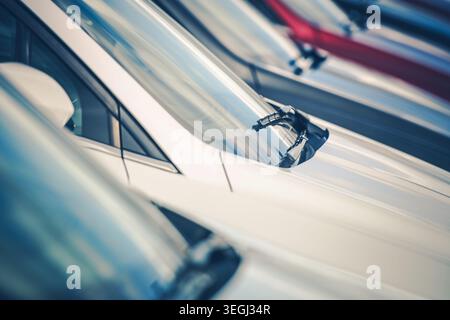 Several cars are parked in a lot during daytime. The focus is on the windshield wipers of a white car. Other cars are visible in the background. The s Stock Photo