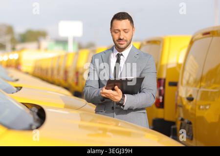 Businessman writing on a clipboard in front of a yellow van fleet Stock Photo