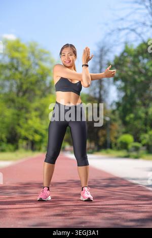 Young woman stretching her arm on a running track on a beautiful sunny day in a park Stock Photo