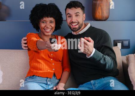 Happy couple sitting on sofa and watching television at home Stock Photo