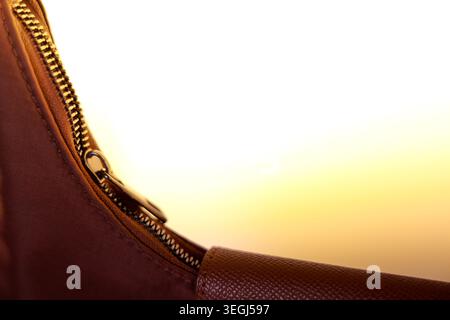 Macro detail showing calm warm gold zipper on brown leather bag accessory. Close metal texture gives an elegant secure feeling against bright blank ba Stock Photo