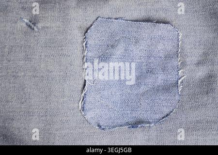 Closeup texture of light blue denim jeans with a stitched fabric patch for repair. Stock Photo