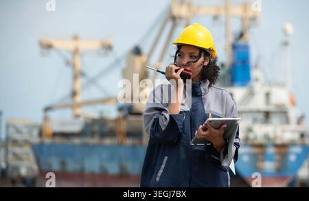 Female maritime engineer using digital tablet for logistics management and industrial port operations near cargo vessel Stock Photo