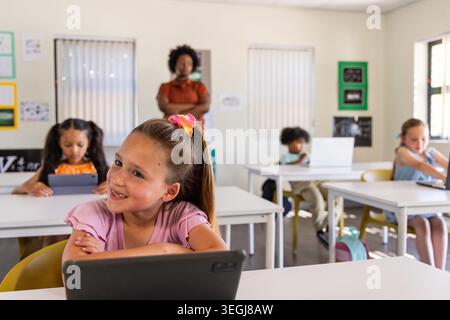 African American teacher watching school age children using tablets and laptop in classroom. Students, devices, edtech, learning, education, educator, focused Stock Photo