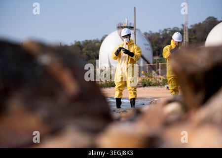 Scientists in yellow suits are collecting water samples from the coastline, flowing away from an oil refinery, before taking the water to the laboratory for further analysis Stock Photo