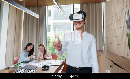 Asian man using virtual reality headset with controller in modern office. Stock Photo
