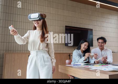 Asian woman using virtual reality headset with controller in modern office. Stock Photo