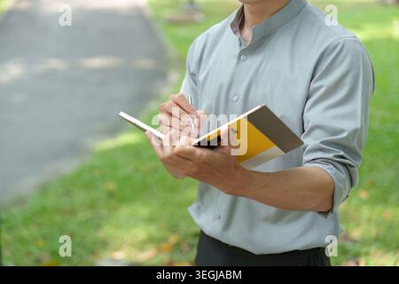 Asian man writing notes in notebook outdoors in park Stock Photo