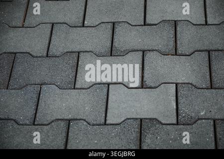 Top down view of grey interlocking dog bone shape concrete paving stones on a walkway. Stock Photo