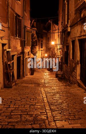 Narrow cobblestone street with old buildings illuminated by warm street lamps in Grisia Street, Rovinj, Croatia. Stock Photo