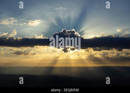 Spectacular sun rays streaming through dramatic storm clouds over a vast desert valley landscape at sunset. Golden light beams illuminate layered moun Stock Photo