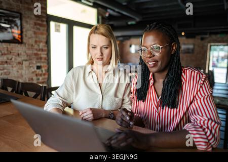 Diverse women collaborating on laptop in coffee shop Stock Photo
