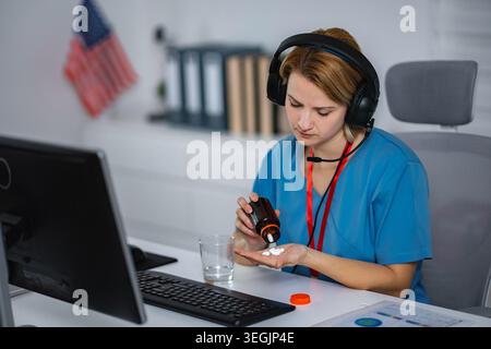 Healthcare worker taking pills at desk wearing headset Stock Photo