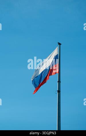 National flag of the Russian Federation waving on a high metal flagpole against a clear bright blue sky on a sunny day. Stock Photo