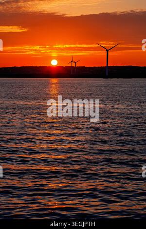 Wind Turbines at sunset on a coast with water reflections Stock Photo