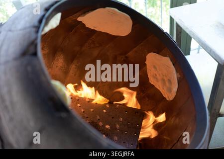 Traditional flatbread dough baking inside a hot clay oven with open flames in Jordan. Middle Eastern cuisine and authentic bread-making process in a t Stock Photo