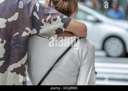 Young couple share tender moment on busy city street. With his arm gently draped over her shoulder, their effortless closeness embodies GenZ romance. Stock Photo